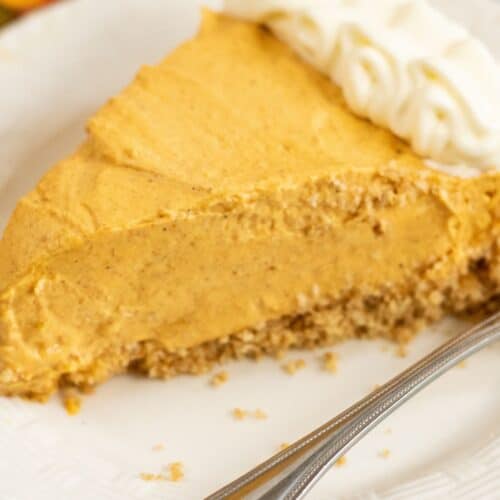 A slice of creamy Cream Cheese Pumpkin Pie with a graham cracker crust and whipped cream on a white plate with a spoon.