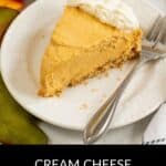 A slice of Cream Cheese Pumpkin Pie with gingersnap crust, topped with whipped cream, sits on a white plate beside a fork.