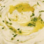 A serving of whipped potatoes topped with melted butter and garnished with chopped chives.