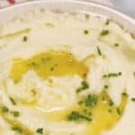 A bowl of whipped potatoes topped with melted butter and finely chopped chives.