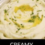 A bowl of creamy whipped potatoes topped with melted butter and chopped chives, with a red and white striped cloth in the background showcases classic comfort food at its finest.