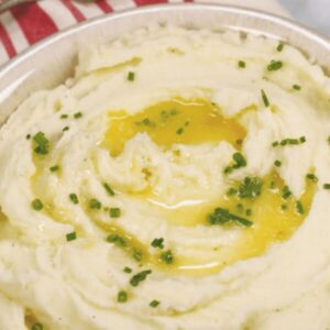 A bowl of whipped potatoes topped with melted butter and chopped chives.