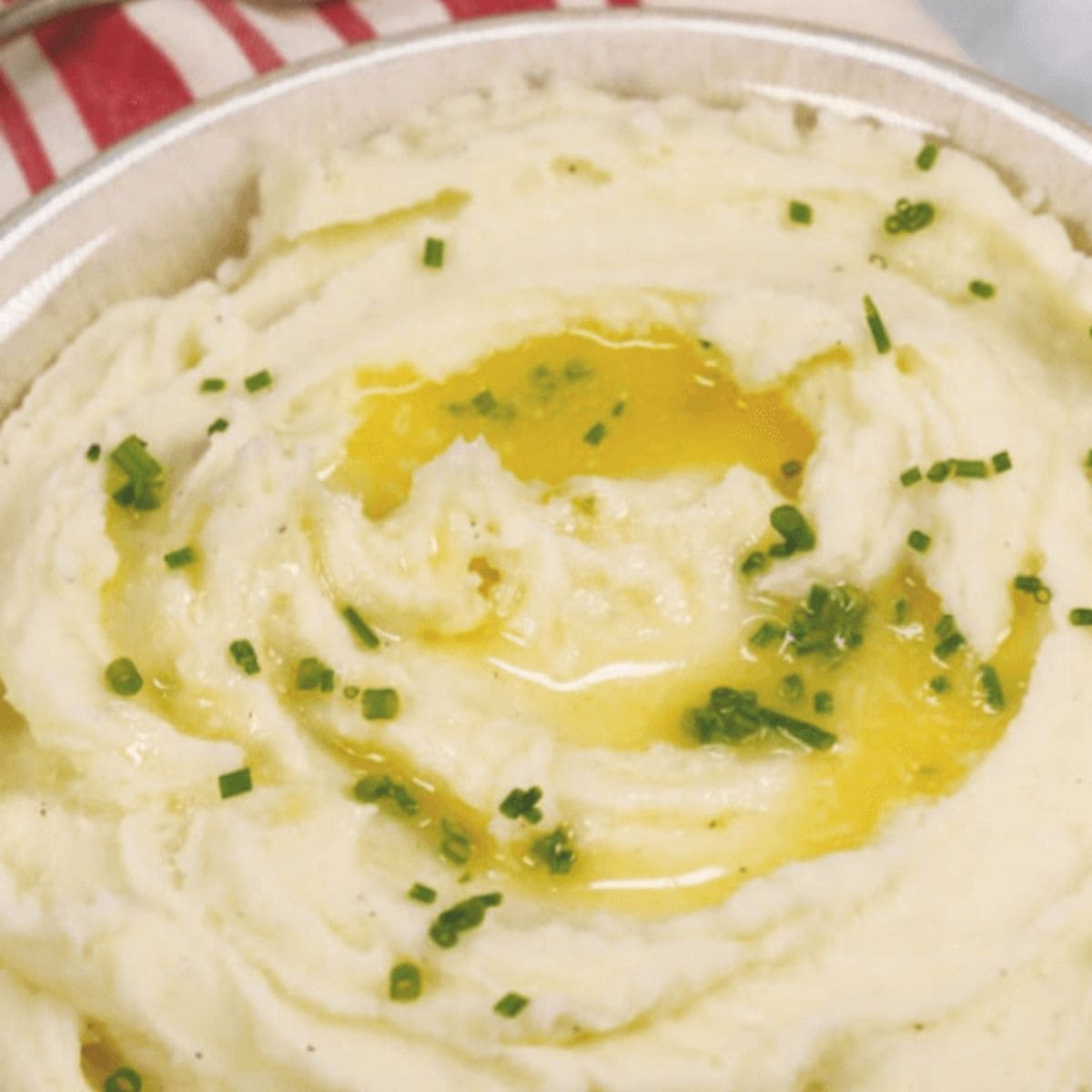 A bowl of whipped potatoes topped with melted butter and chopped chives.