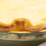 Close-up of a baked pie with a golden, crimped Crisco Pie Crust in a clear glass pie dish, next to a red and white striped cloth.
