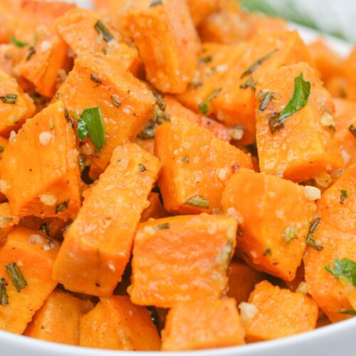 A bowl of roasted sweet potato cubes garnished with chopped herbs and seasoning, this savory sweet potatoes recipe makes a delicious and flavorful side dish.