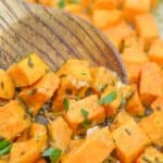 Cubed roasted sweet potatoes with herbs and minced garlic are stirred with a wooden spoon in this savory sweet potatoes recipe.
