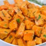 A white bowl filled with roasted sweet potato cubes garnished with chopped herbs, likely rosemary and parsley—an inviting Savory Sweet Potatoes Recipe perfect for any meal.