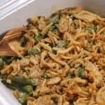 A Crock Pot Green Bean Casserole topped with crispy fried onions in a white baking dish, with a wooden spoon on the side.