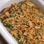 A side topped with crispy fried onions is served in a white baking dish, with a wooden serving spoon on the side.