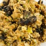 A close-up of Crock Pot Stuffing with mushrooms, celery, and herbs served on a white plate with a decorative border.