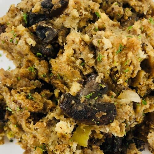 A close-up of a serving of Crock Pot Stuffing with mushrooms, herbs, and vegetables on a white plate with a dotted border.