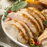 Sliced Crock Pot Turkey Breast garnished with herbs and orange zest, served on a white plate.