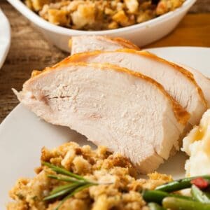 Two thick slices of Crock Pot Turkey Breast on a plate with stuffing, mashed potatoes, and green beans.