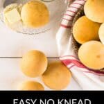 A hand spreads butter on a roll beside a basket of No Knead Rolls, a glass bowl with butter, and a red-striped towel. Text reads, "Easy No Knead Rolls.