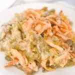 A serving of French’s Green Bean Casserole topped with crispy fried onions sits on a white plate.