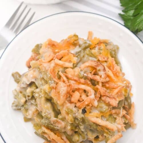 A serving of French’s Green Bean Casserole topped with crispy fried onions sits on a white plate.