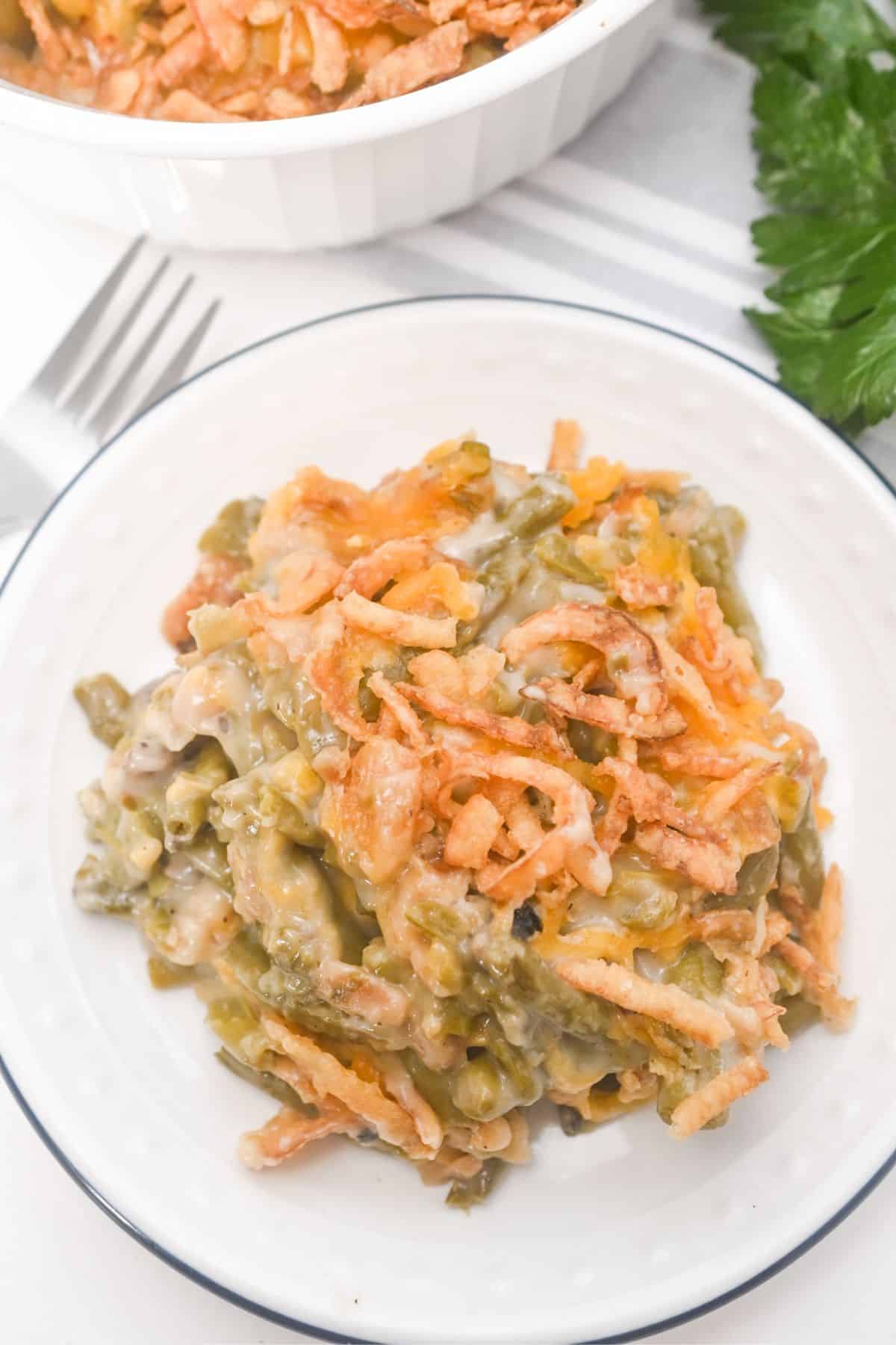 A serving of French’s Green Bean Casserole topped with crispy fried onions sits on a white plate.
