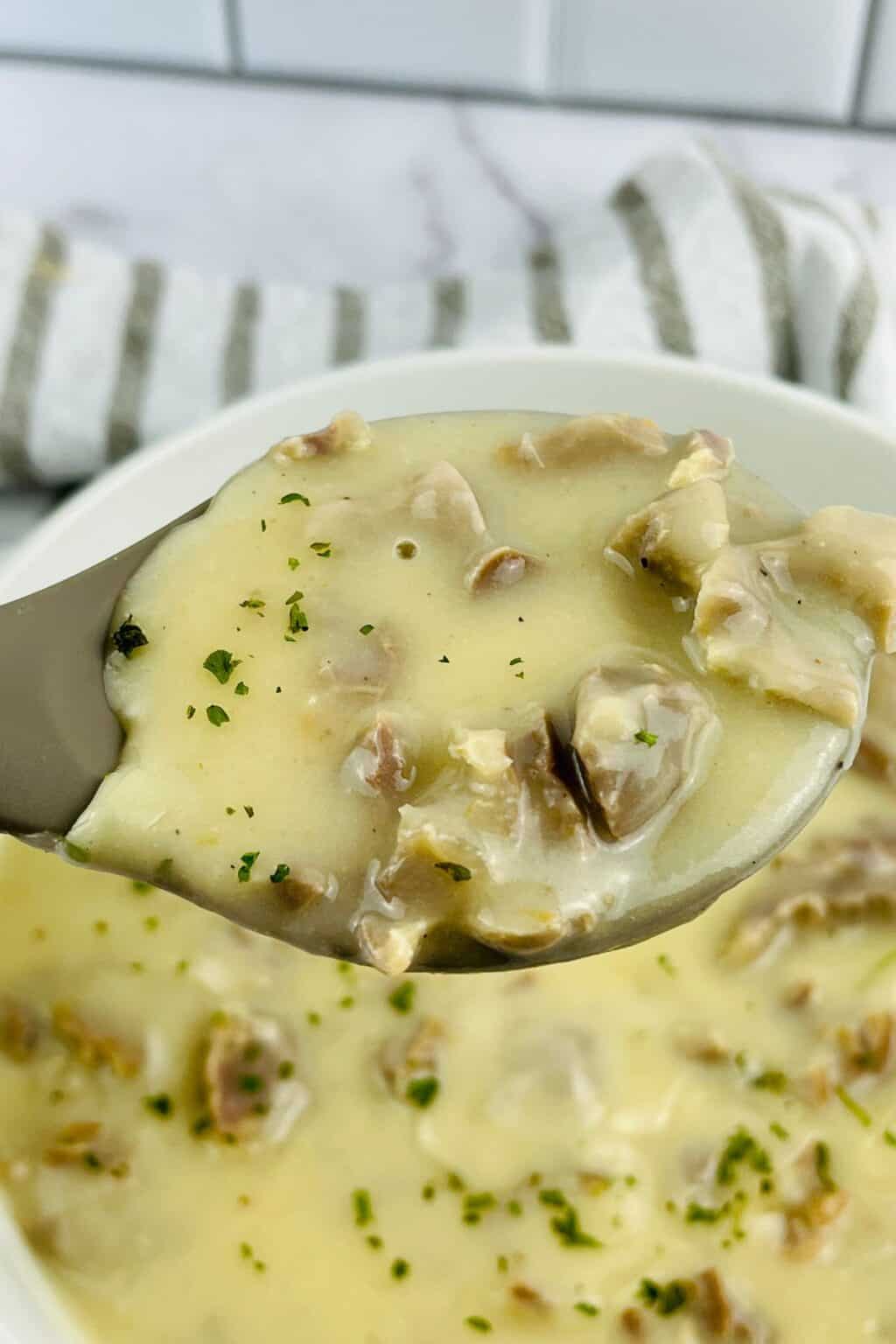 A spoonful of creamy mushroom soup garnished with herbs, held above a bowl of the same soup—perfect alongside rich turkey neck gravy.