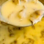 A close-up of a ladle holding creamy Turkey Neck Gravy with chunks of chicken, suspended over a pot filled with more savory gravy.