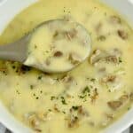 A bowl of creamy soup with chunks of mushrooms, finished with herbs and a hint of rich Turkey Neck Gravy, with a spoon resting inside the bowl.