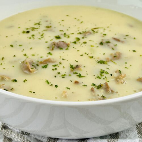 A bowl of creamy soup with visible mushroom pieces, garnished with chopped herbs and a hint of savory Turkey Neck Gravy, placed on a striped cloth.