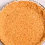 A glass pie dish filled with an unbaked, evenly pressed Graham Cracker Pie Crust sits on a light surface, ready for your favorite filling.