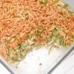 A glass baking dish with Green Bean Casserole without Mushroom Soup, topped with crispy fried onions, showing a portion removed.