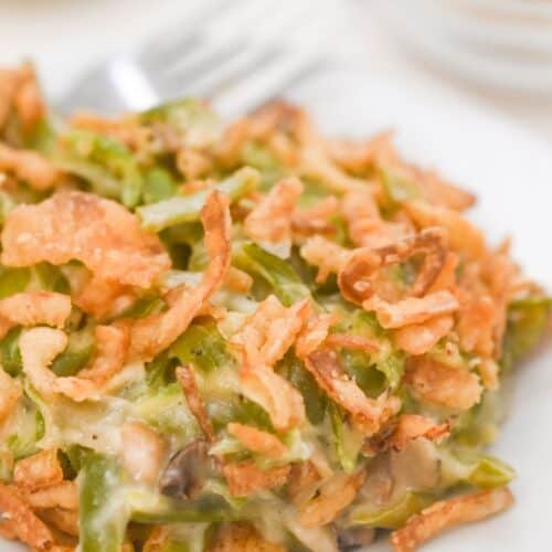 A serving of Green Bean Casserole without Mushroom Soup topped with crispy fried onions on a white plate.