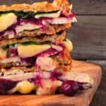 Close-up of a stacked sandwich with melted cheese on a rustic wooden board, set against a wooden background.