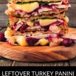A stacked Turkey Panini with melted cheese, cranberry sauce, and greens on toasted bread sits on a wooden board. Text reads: "Leftover Turkey Panini Thanksgiving Day Sandwich.