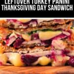 Close-up of a Turkey Panini sandwich with melted cheese, cranberry sauce, and spinach on a wooden cutting board. Text above reads "Leftover Turkey Panini Thanksgiving Day Sandwich.