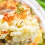 A close-up of a cheesy cauliflower casserole with a golden-brown crust and green onions on top, held invitingly in a serving spoon.