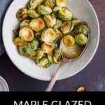A bowl of Maple Glazed Brussels Sprouts with a spoon, placed on a dark surface, showcases this sweet and savory side dish.