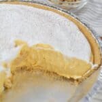 A finished desert with creamy filling, and whipped topping, with a slice removed. A bowl of walnuts is in the background.