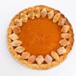 An Old Fashioned Pumpkin Pie with a golden crust, decorated with small leaf-shaped pastry pieces around the edge, sits on a white background.