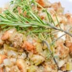 A bowl of Old Fashioned Stuffing with celery and onions, garnished with a sprig of fresh rosemary and thyme.