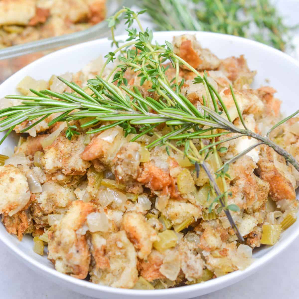 A bowl of Old Fashioned Stuffing with chopped celery and onions, garnished with fresh rosemary and thyme sprigs.