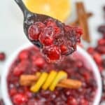 A close-up of a spoonful held above a bowl, with a cinnamon stick, and a lemon slice in the background.