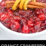 A bowl of Orange Cranberry Sauce garnished with cinnamon sticks and twisted orange peel, with "Orange Cranberry Sauce" text displayed at the bottom.