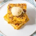 Pumpkin Crunch Cake, are stacked on a white plate and topped with a scoop of vanilla ice cream, set atop a patterned cloth.