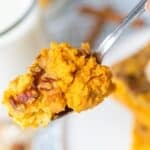 A close-up of a spoonful with pecans, held above a plate, with a glass of milk in the background.