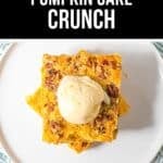 A square slice of Pumpkin Crunch Cake topped with a scoop of vanilla ice cream sits on a white plate.