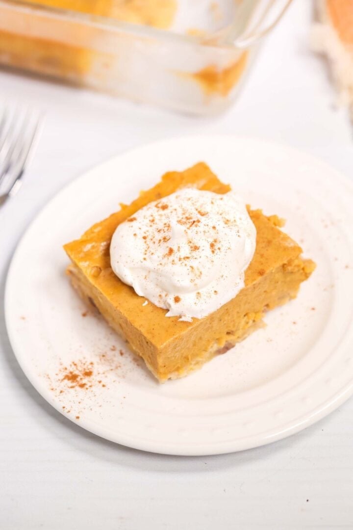A square piece of Pumpkin Pie Dessert Bar topped with whipped cream and a sprinkle of cinnamon sits on a white plate.