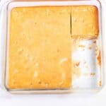 A square baking dish with golden-brown Pumpkin Pie Dessert Bars, one corner piece removed to reveal the smooth, creamy texture of the interior.