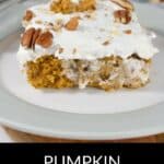 A slice of Pumpkin Poke Cake topped with white frosting and chopped pecans sits on a white plate.