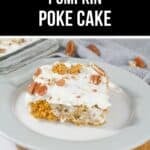 A slice of Pumpkin Poke Cake topped with white frosting and pecans sits on a white plate, while a baking dish of the cake is seen in the background.