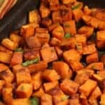 Cubes roasted with herbs on a black baking tray.