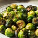 A plate of roasted Brussels sprouts with browned, crispy edges, topped with savory Parmesan cheese, served on a white dish.