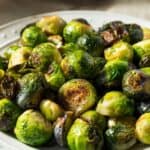 A white plate filled with Roasted Brussels Sprouts with Parmesan Cheese, showing browned and caramelized edges.