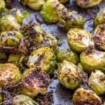 Roasted Brussels Sprouts with Parmesan Cheese, halved and browned to perfection with herbs and seasoning, are spread on a baking tray for a flavorful side dish.